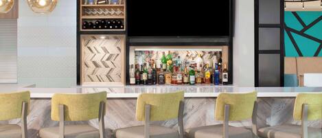 A bar area with a marble herringbone floor, bar stools, a variety of liquor bottles, and pendant lighting.