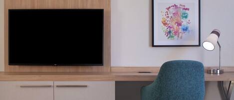 Et moderne værelse med et fladskærms-tv, et skrivebord med stol, et indrammet abstrakt maleri og en skrivebordslampe.