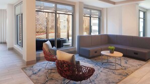 Una sala de estar moderna con un sofá gris, sillas de mimbre rojas, una mesa de centro redonda y grandes ventanas que ofrecen vistas a muebles de exterior.