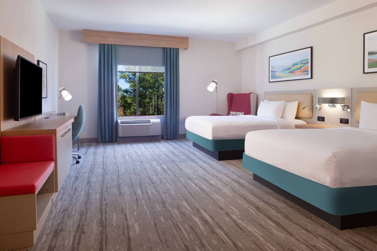 Une chambre d’hôtel avec deux lits, un bureau, une télévision et une fenêtre avec des rideaux.