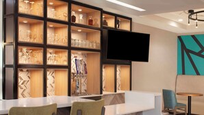 Zona de bar con estantes llenos de vasos y botellas, un televisor de pantalla plana y asientos.