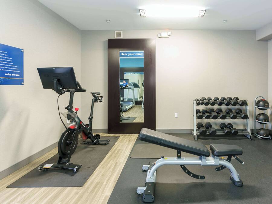 A gym with exercise equipment, a bench, and a rack of dumbbells.