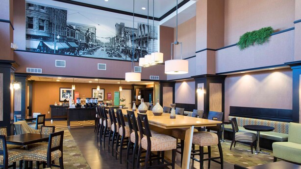 A hotel lobby with a long dining table, multiple chairs, a bar area, and a seating area with sofas and chairs. - Hampton Inn & Suites Danville (Danville)
