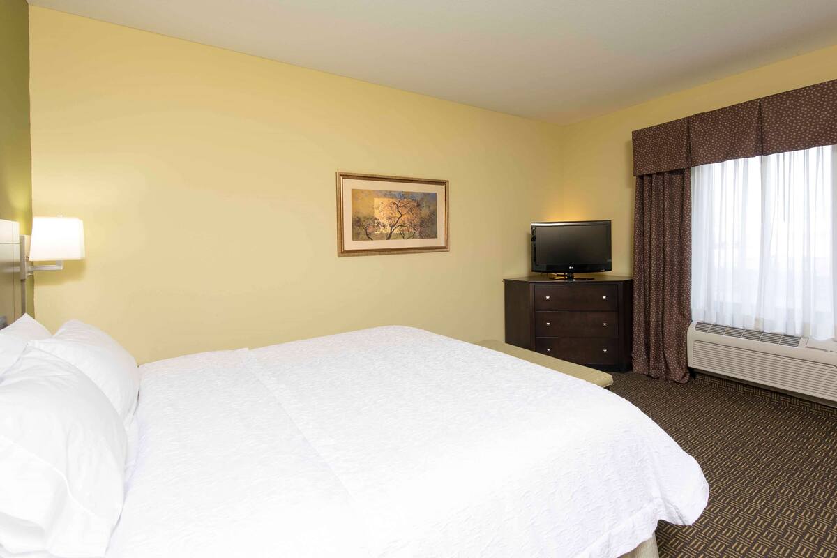 Una habitación de hotel con una cama grande, un televisor en una cómoda y una ventana con cortinas.
