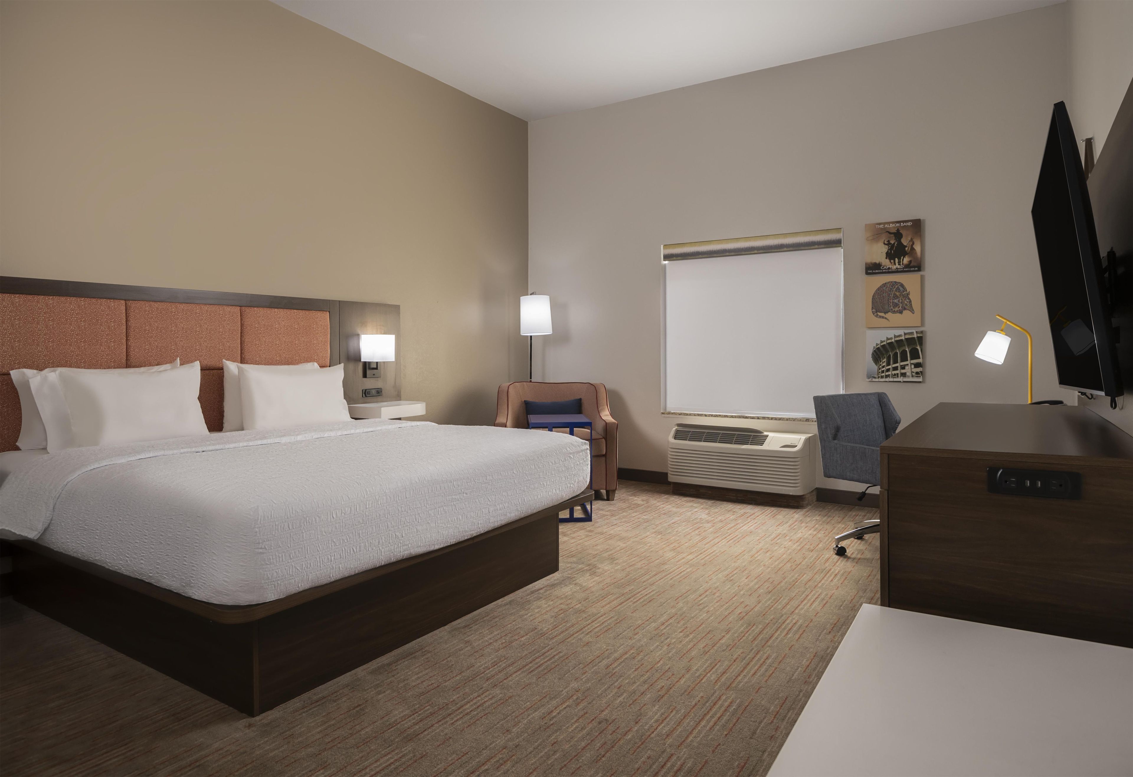 A hotel room with a large bed, a desk, a chair, a flat-screen TV, and a window.