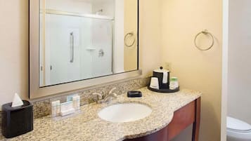 Un baño con lavamanos de encimera de granito, espejo, toallero y estación de café.