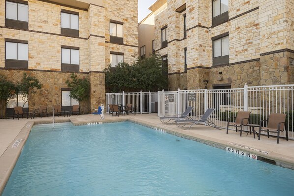 A swimming pool with lounge chairs and a fenced area, surrounded by stone buildings.