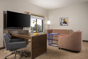Une chambre d’hôtel équipée d’un bureau, d’une télévision, d’un canapé, d’une chaise, d’une lampe et d’une fenêtre.