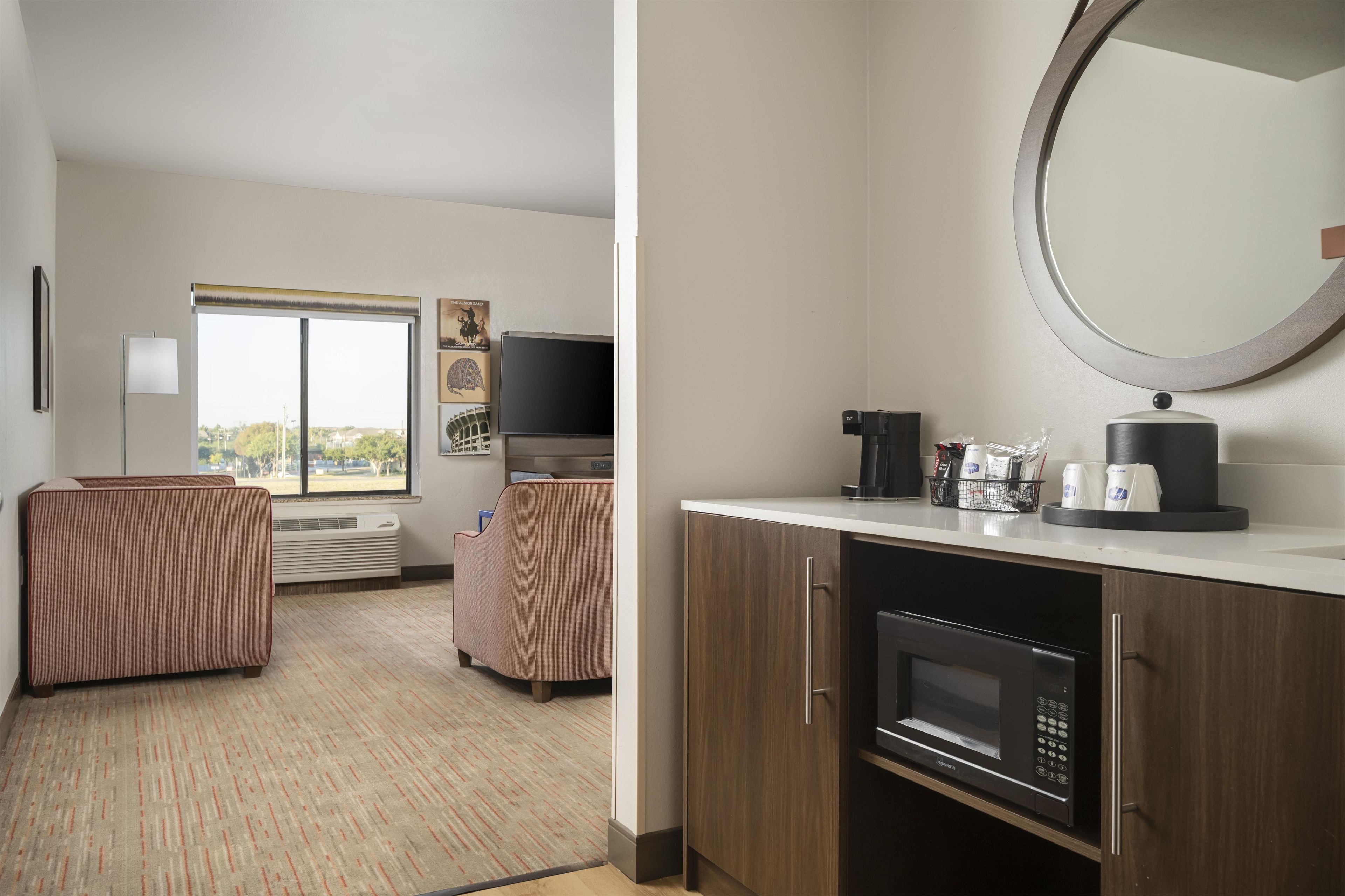 A hotel room with a kitchenette, a flat-screen TV, a sofa, a window with a view, and a mirror.