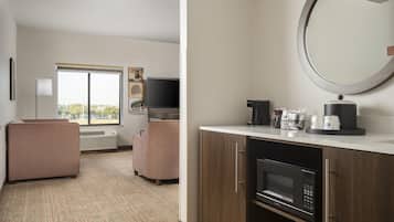 A hotel room with a kitchenette, a flat-screen TV, a sofa, a window with a view, and a mirror.