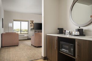 Habitación de hotel con kitchenette, televisor de pantalla plana, sofá, ventana con vistas y espejo.