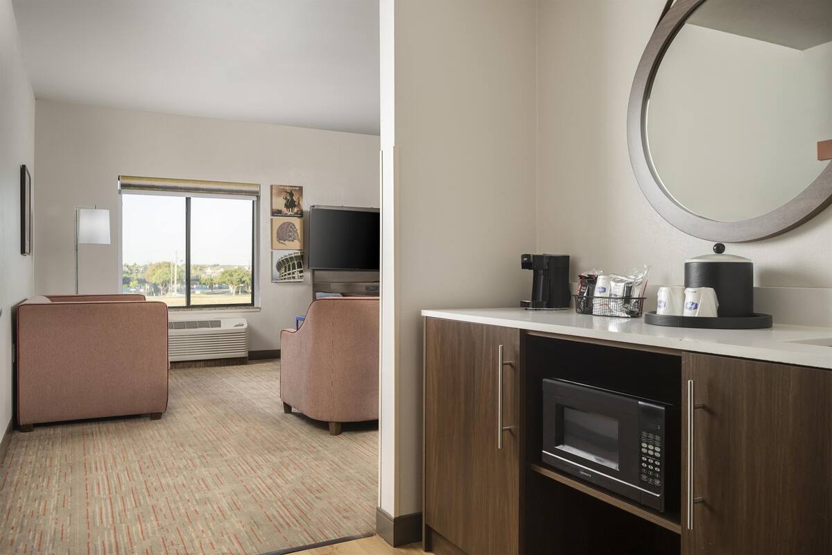 A hotel room with a kitchenette, a large window, a flat-screen TV, and a seating area with a sofa and armchair.