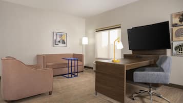 A hotel room with a sofa, a desk, a chair, a television, and a window.