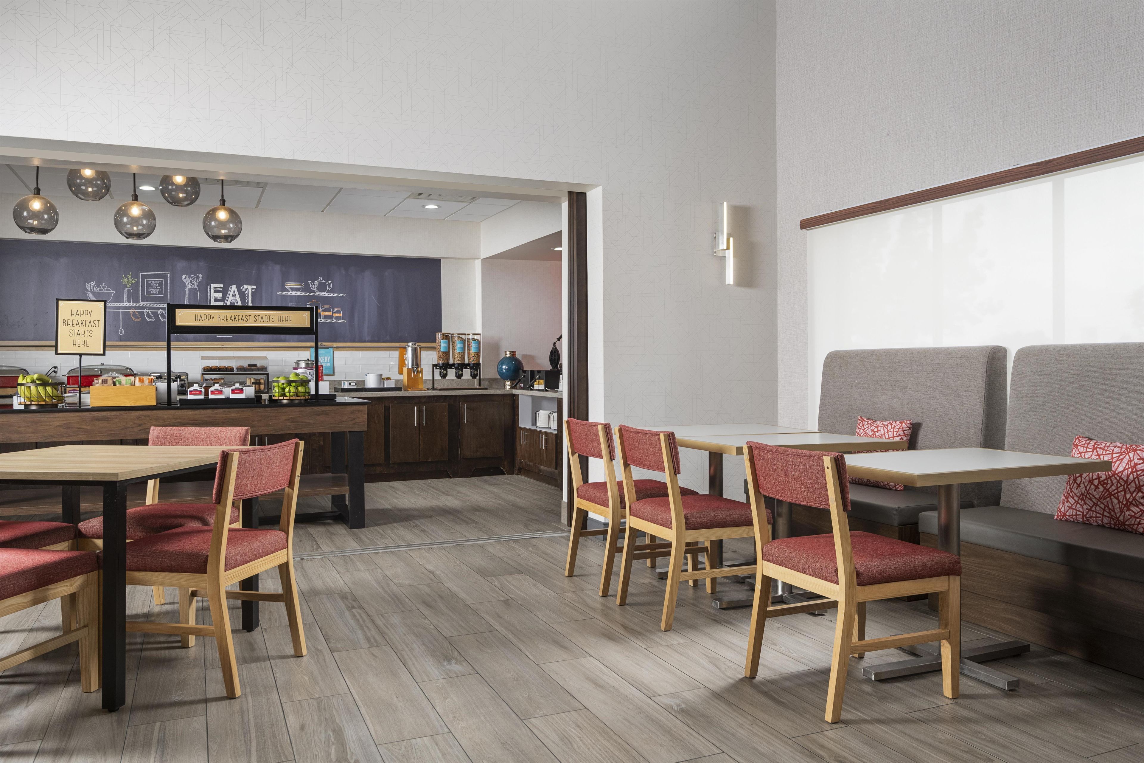 Un café moderne avec des tables et des chaises en bois, un tableau noir servant de menu et un coin bar.