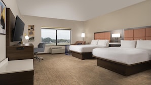 A hotel room with two beds, a desk, a chair, a television, and a window with a view.
