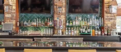 A bar with a stone wall, two TVs, and a variety of liquor bottles.