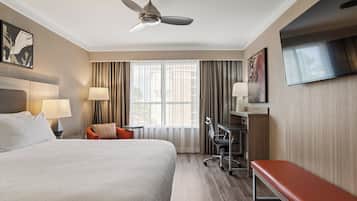 Een hotelkamer met een groot bed, een bureau met stoel, een aan de muur bevestigde televisie en een plafondventilator.