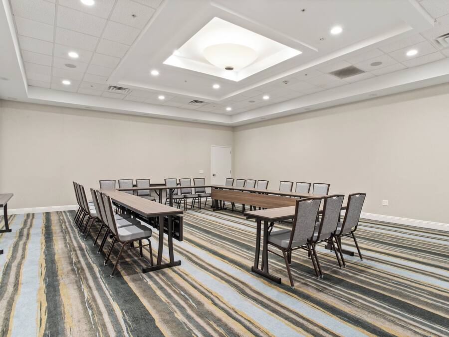 Un salón de conferencias con una larga mesa y sillas, piso alfombrado, paredes blancas e iluminación empotrada en el techo.