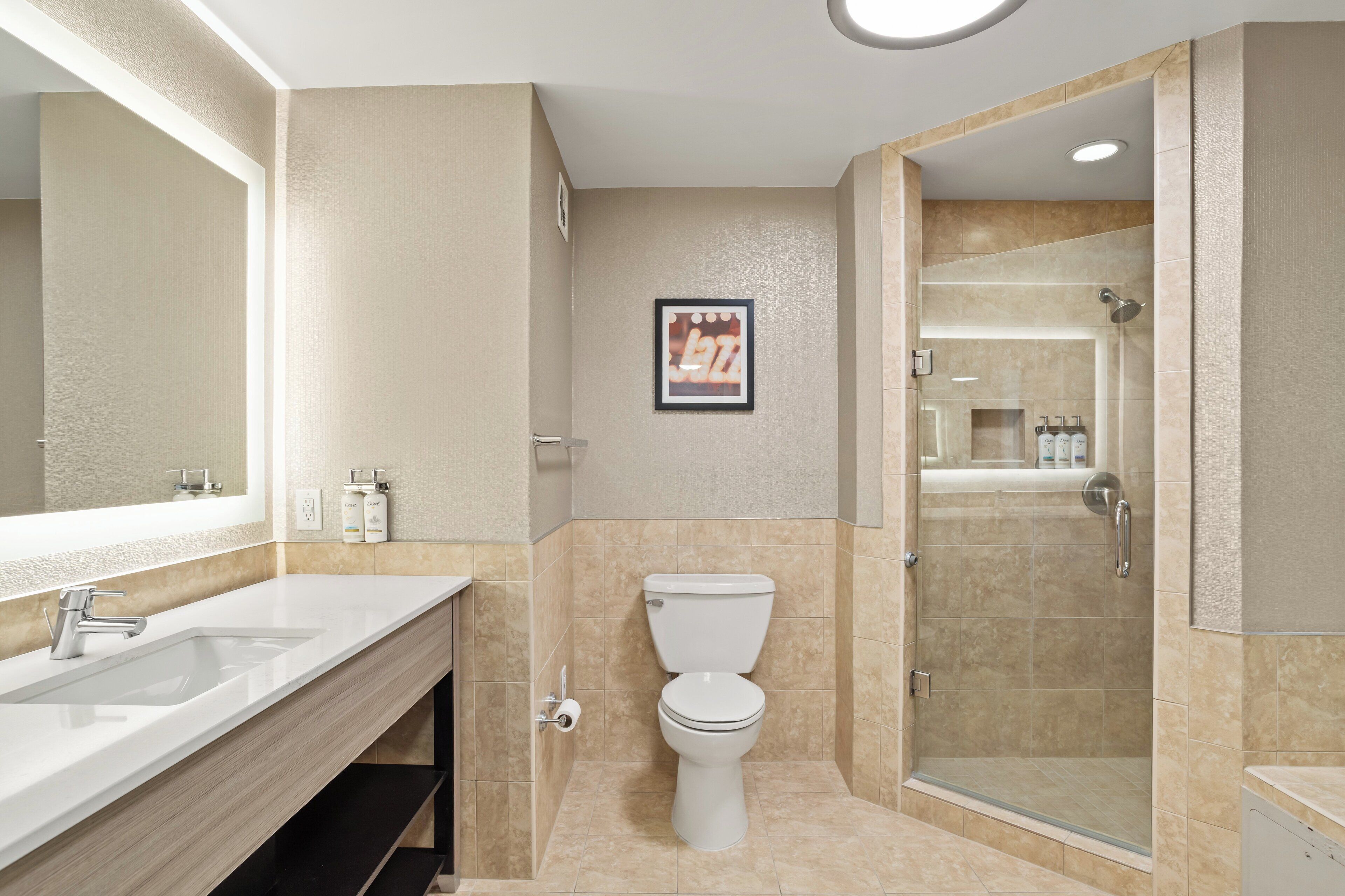 A modern bathroom with a large mirror, two sinks, a toilet, and a glass-enclosed shower.