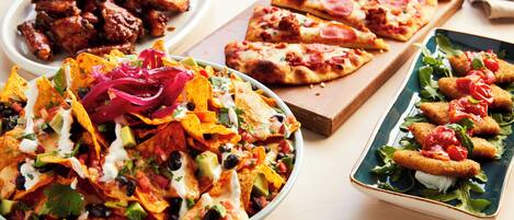 Une variété de plats, notamment des nachos, des pizzas et des aliments frits, sont disposés sur une table.