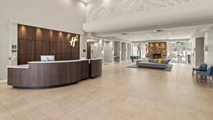 Un hall d’hôtel moderne comprenant un comptoir d’accueil, un espace salon et une cheminée.