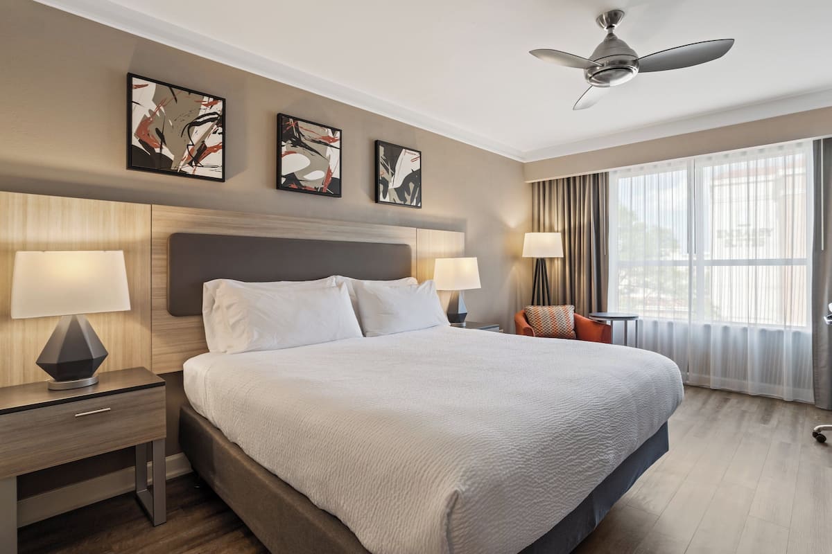 A hotel room with a large bed, two bedside tables with lamps, a ceiling fan, and artwork on the walls.