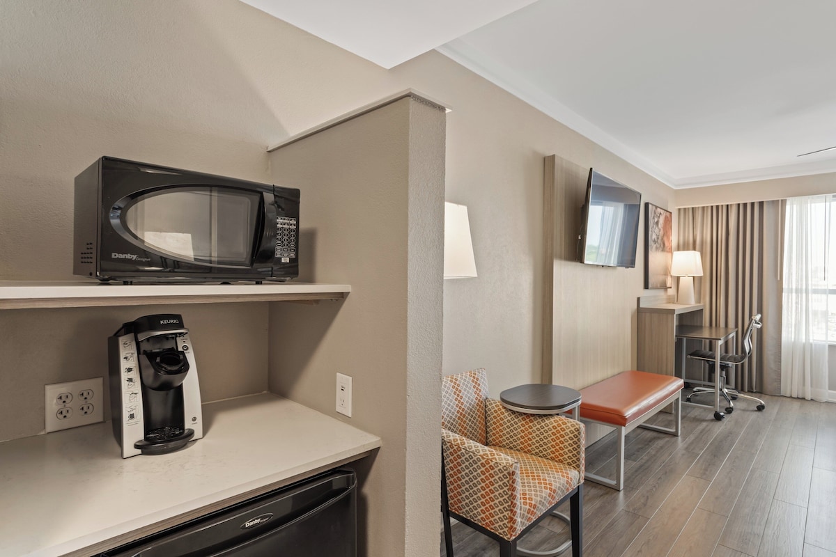 Ein Hotelzimmer mit Küchenzeile, einer Mikrowelle, einer Kaffeemaschine, einem Fernseher, einem Sessel, einem Tisch und einer Lampe.