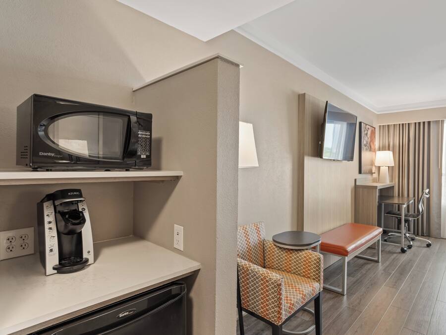 A hotel room with a kitchenette, a microwave, a coffee maker, a TV, a chair, a table, and a lamp.