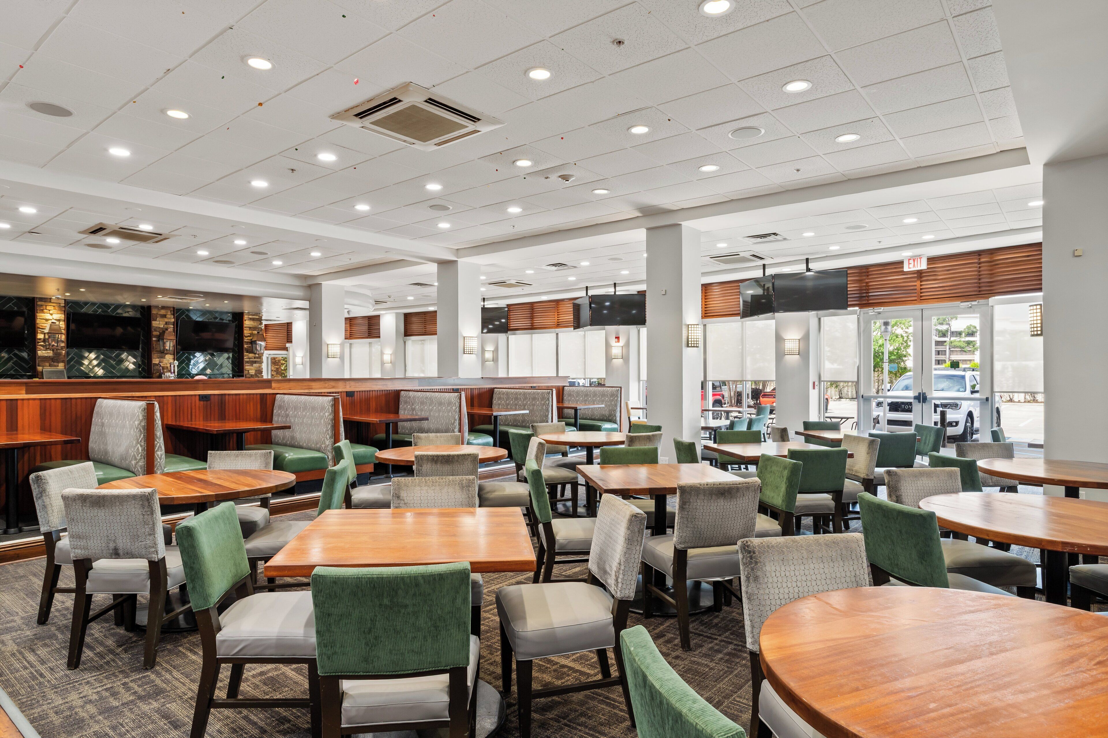A spacious indoor seating area with multiple tables and chairs, a counter with a menu display, and a view of the outside through large windows.