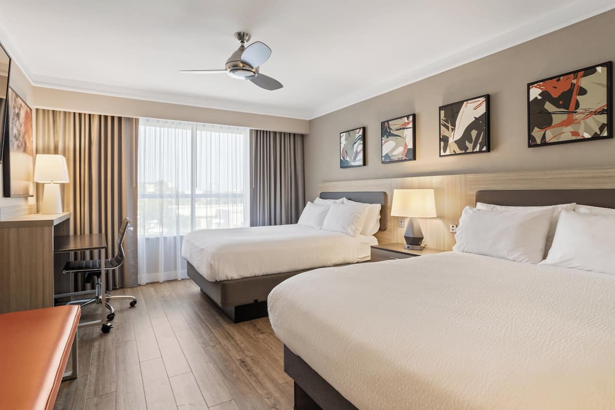 A hotel room with two beds, a desk, a chair, and a ceiling fan.