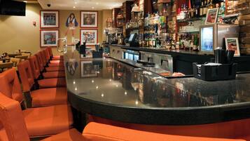A bar area with a curved counter, seating with orange cushions, and a variety of bottles and glasses on shelves.