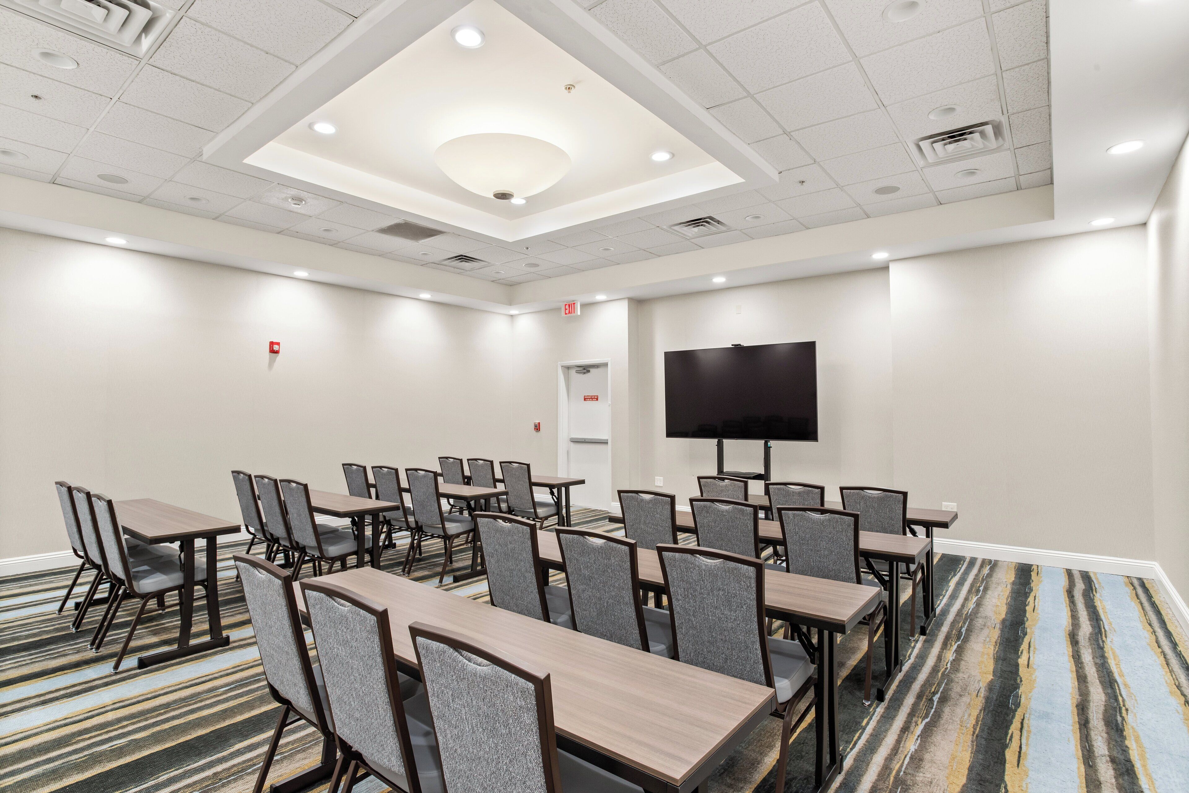 A conference room with tables and chairs, a flat-screen TV, and a carpeted floor.