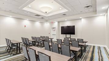A conference room with tables and chairs, a flat-screen TV, and a carpeted floor.