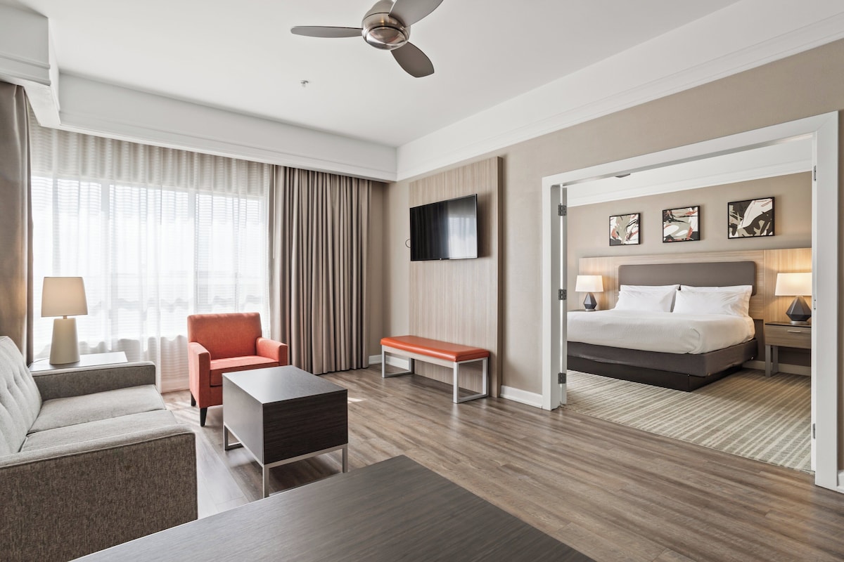 Ein Hotelzimmer mit Bett, Schreibtisch, Stuhl, Fernseher und Deckenventilator.