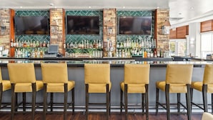 Un espace bar avec un mur en pierre et en bois, plusieurs téléviseurs et un grand choix de bouteilles.