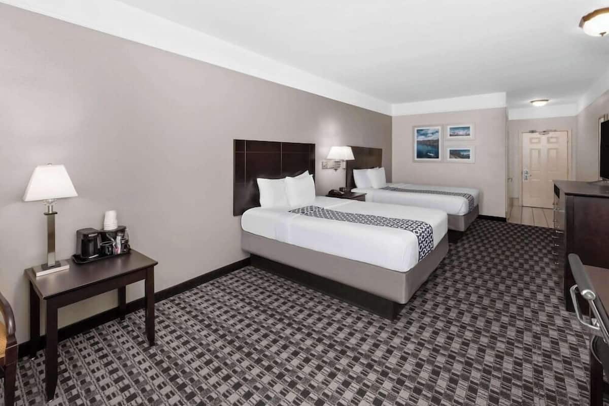 A hotel room with two beds, a desk with a lamp, a coffee maker, and a door.
