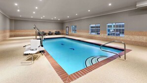 An indoor swimming pool with a wheelchair-accessible lift, a pool ladder, and a view of a building through the windows.
