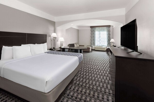 A hotel room with a large bed, a desk, a chair, a television, and a sofa.