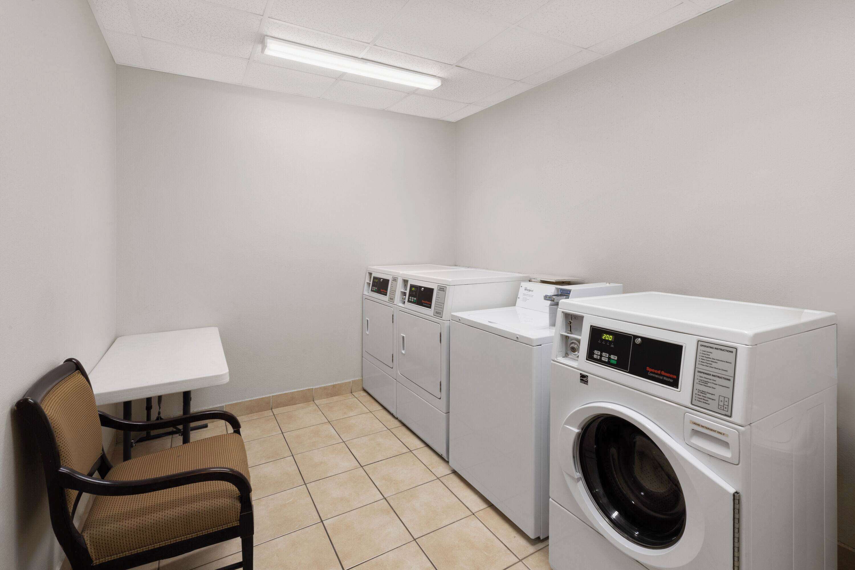 A laundry room with a washing machine, dryer, and a chair.