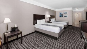 A hotel room with two beds, a desk with a lamp, a coffee maker, and a television.