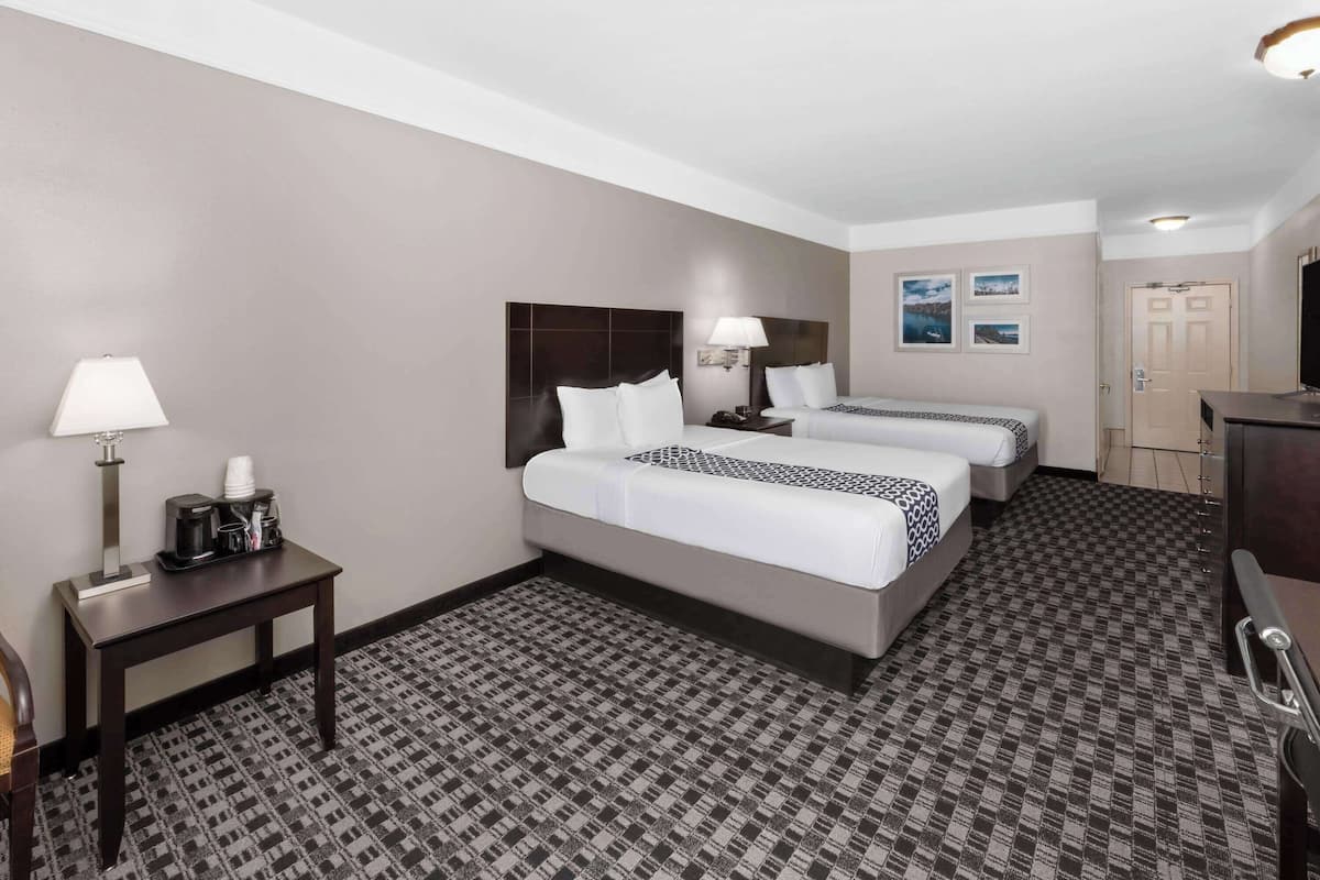 A hotel room with two beds, a desk with a lamp, a coffee maker, and a television.