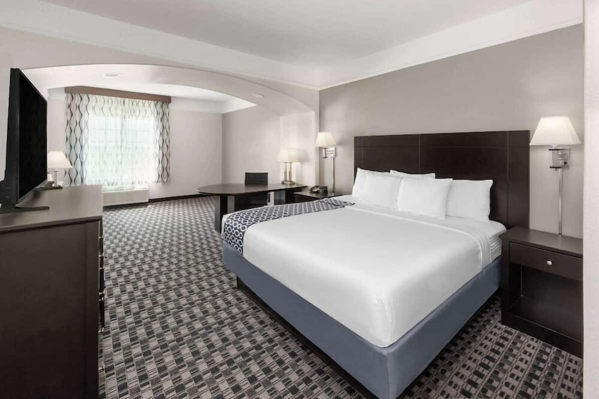 A hotel room with a large bed, a desk, a chair, a TV, and a window with curtains.