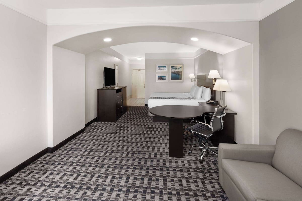 A hotel room with a bed, a desk with a chair, a sofa, a TV, and a lamp.