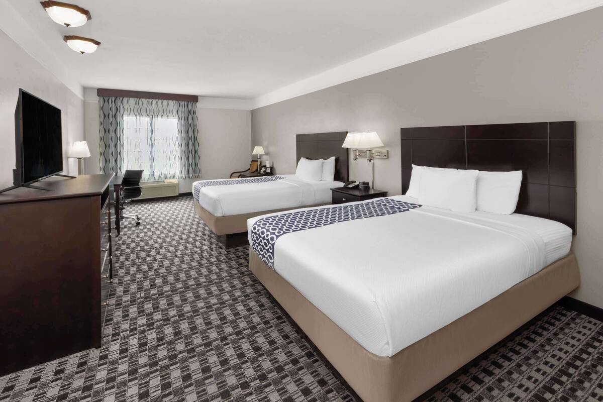 A hotel room with two beds, a desk, a TV, and a patterned carpet.