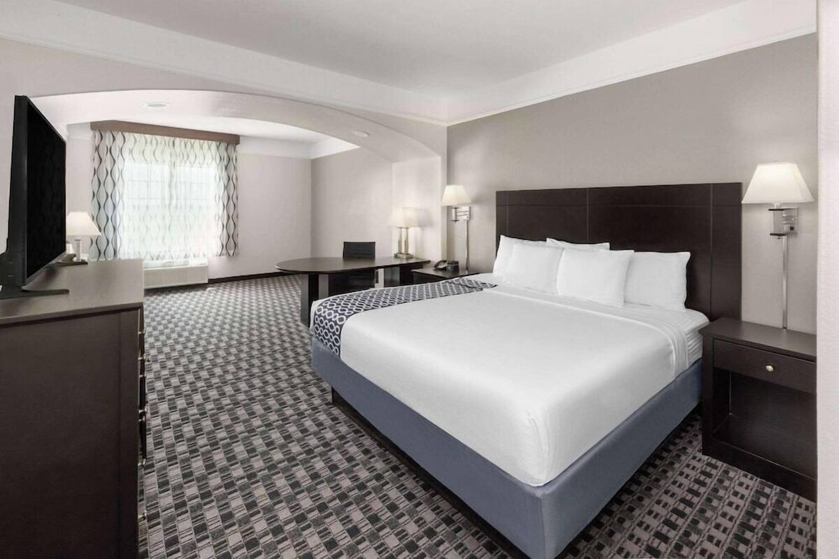 A hotel room with a large bed, a desk, a chair, a TV, and a window with curtains.