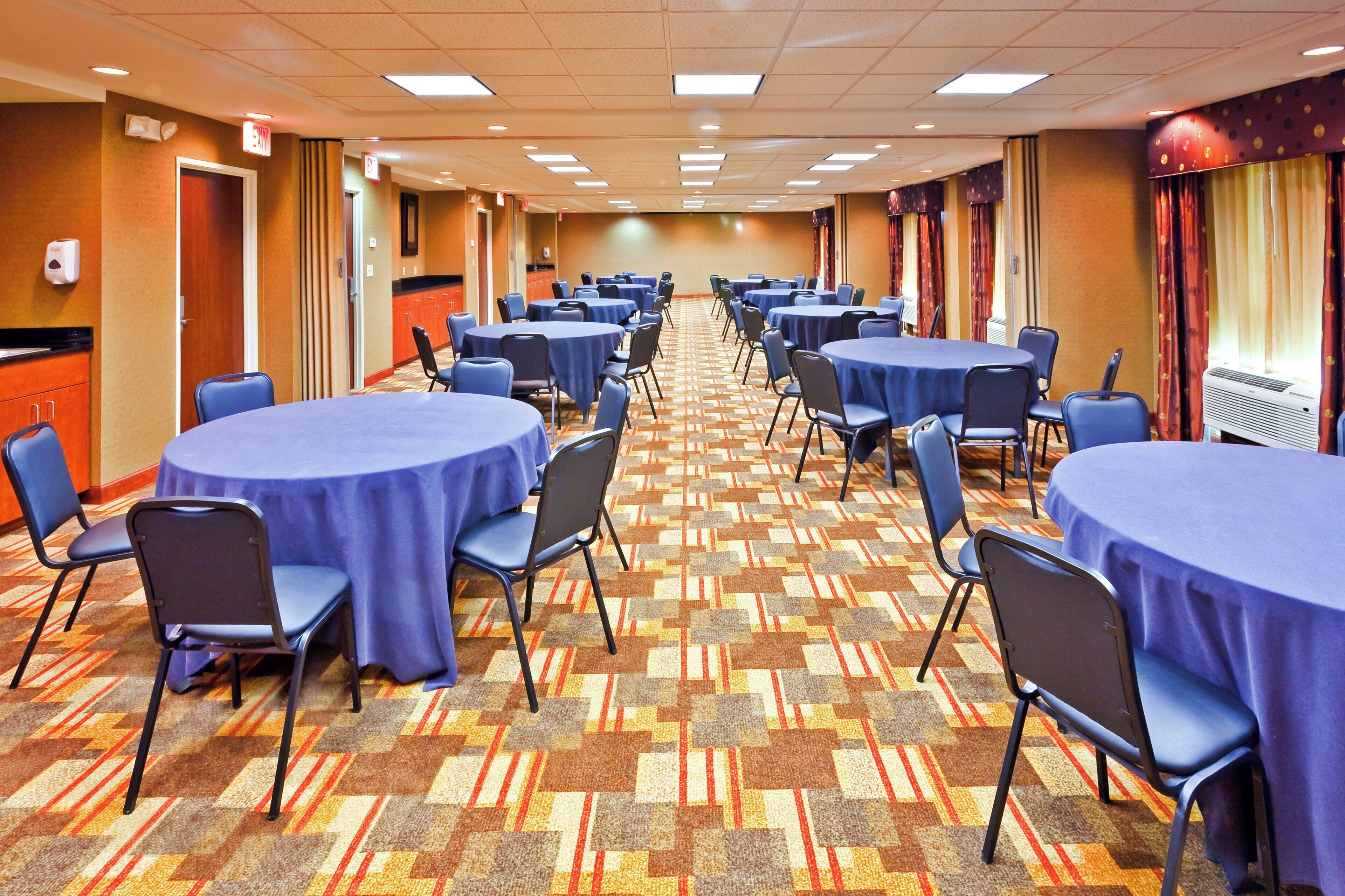 Un salón de conferencias de hotel con varias mesas redondas, sillas y piso alfombrado.