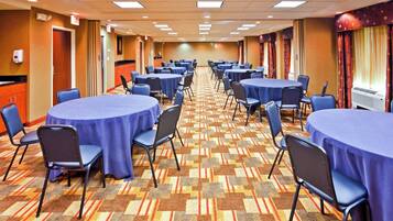Un salón de conferencias de hotel con varias mesas redondas, sillas y piso alfombrado.