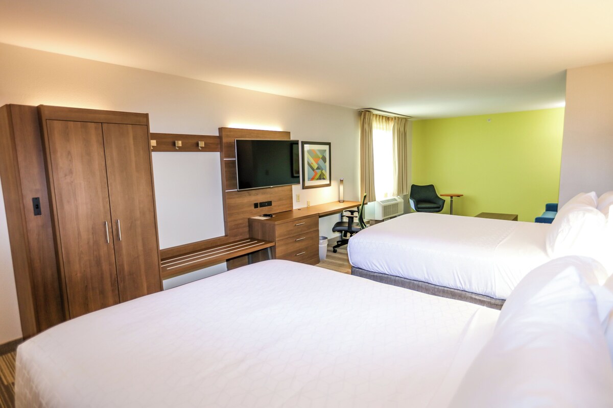 A hotel room with two beds, a desk with a computer, a TV, and a wardrobe.