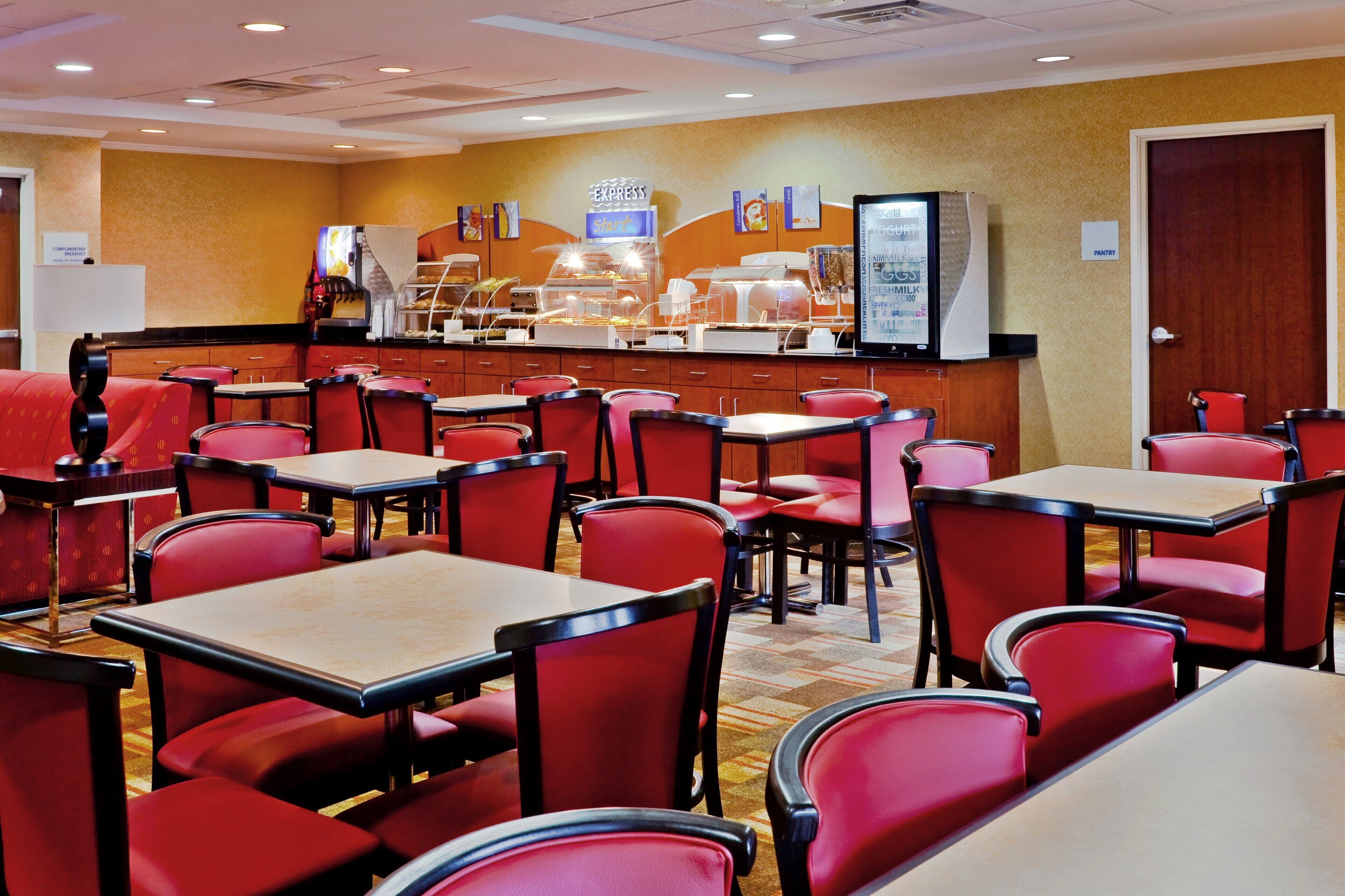 Comedor con sillas y mesas rojas, un mostrador de buffet y un cartel para el buffet exprés.
