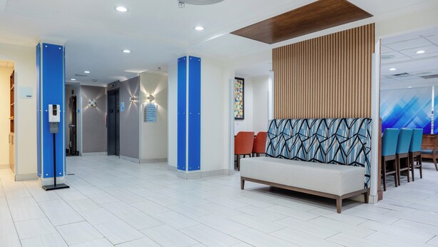 A modern lobby with a reception desk, a seating area with patterned cushions, and a staircase leading to an upper floor.